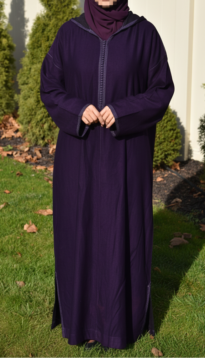 Woman wearing a long dark purple abaya outdoors with greenery in the background